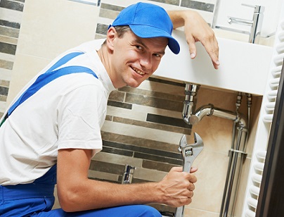 Young happy plumber worker with spanner at sanitary washbasin installation system